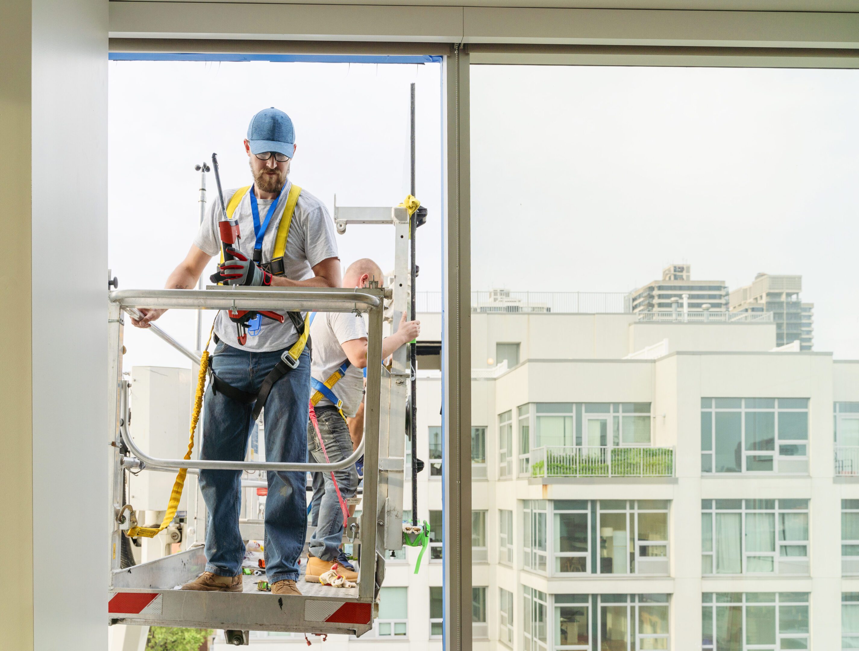 Team of blue-collar workers replacing a broken window in the office building. High-altitude work on the lifting platform which is placed outside.